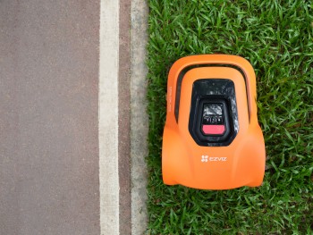 Ezviz RM600 robotmaaier voor slimme gazonverzorging Oranje Ezviz RM600 robotmaaiers in actie op een gazon, met een bestrating ernaast.