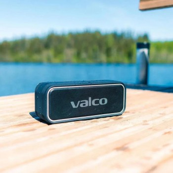 Valco Nordell MK3 luidspreker bij een meerlandschap op houten oppervlak Het Valco-logo van een zwarte rechthoekige luidspreker, geplaatst op een houten oppervlak met een meerlandschap op de achtergrond.